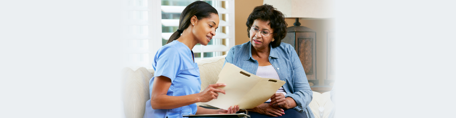Nurse Discussing Records With Senior Female Patient During Home Visit Talking